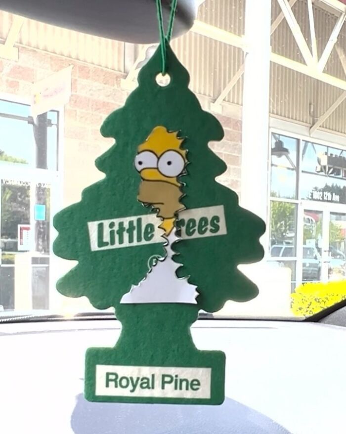 Simpsons paper cutout of a character in a Little Trees air freshener on a car windshield representing real-world art.