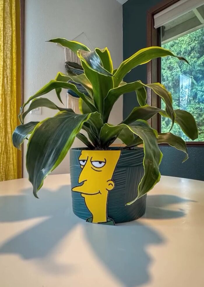 Simpsons paper cutout art placed in a plant pot on a white table with leafy green plant.
