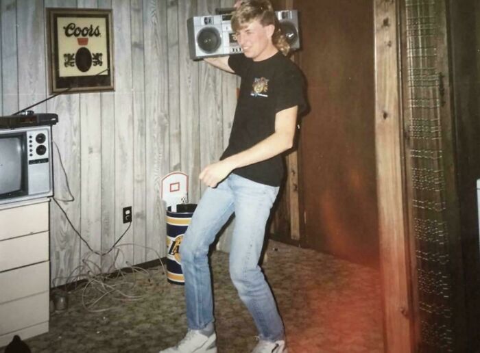 Young man in the 80s holding a boombox on his shoulder, standing in a vintage room. Historical capsule vibe.