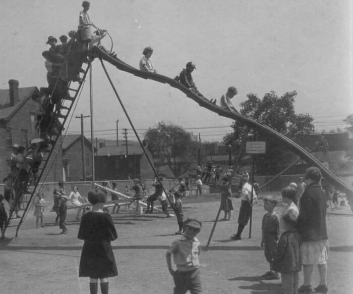 Children playing on a large vintage playground slide, surrounded by onlookers, showcasing historical playground design.