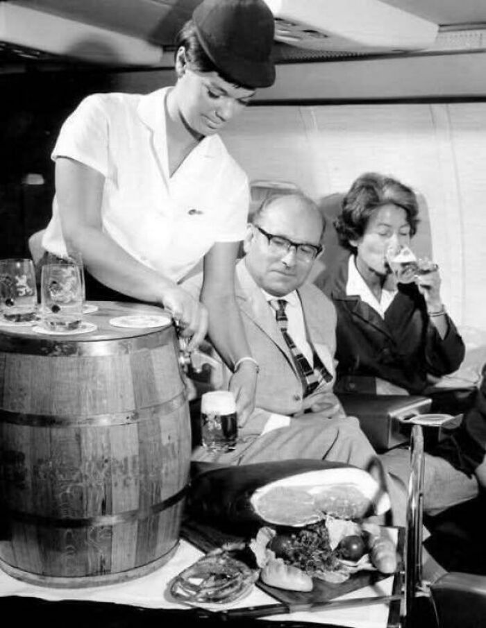 Flight attendant serves beer from a keg to passengers enjoying in-flight dining, showcasing a historical capsule of vintage air travel.