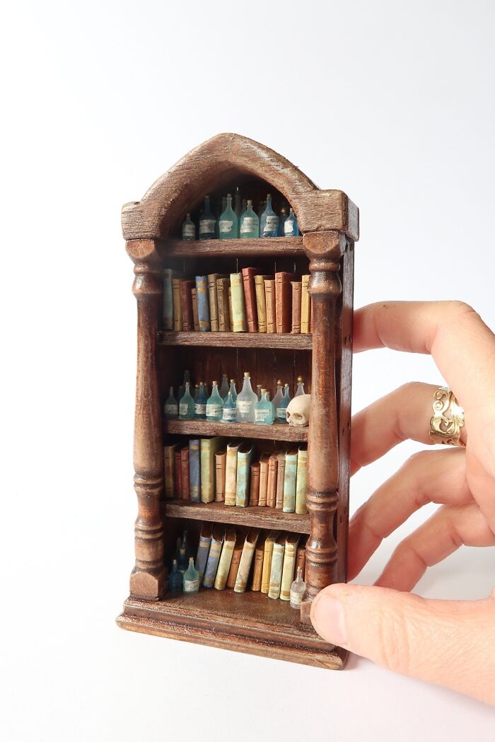 Miniature wooden bookshelf with tiny books and bottles, showcasing Tamar Cohen's mesmerizing miniatures.