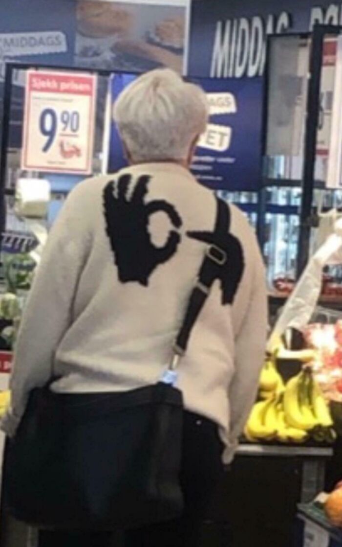 Elderly person wearing a sweater with a playful hand sign design in a grocery store.