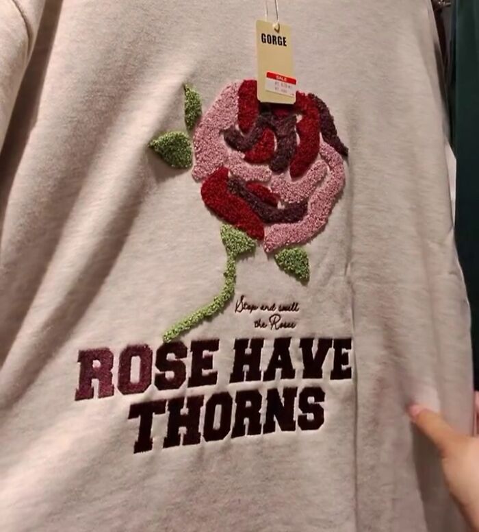 Gray shirt with rose design and poorly translated text, photographed in a Japanese store.