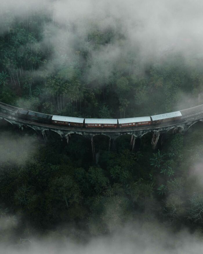 Aerial photo of a train crossing a bridge through misty forest from a different angle.