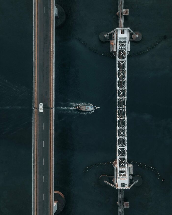 Aerial photo of a bridge with a car and a boat underneath, showing the world from a different angle.