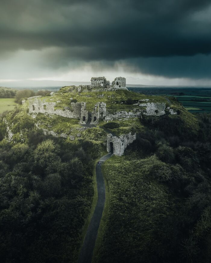 Aerial view of a dramatic ruined castle on a hilltop under dark, stormy skies, showcasing a unique perspective.
