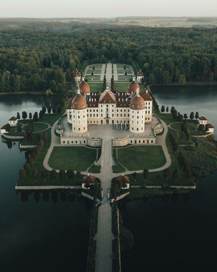 Aerial photo of a grand castle surrounded by water and lush forest, showcasing the world from a different angle.