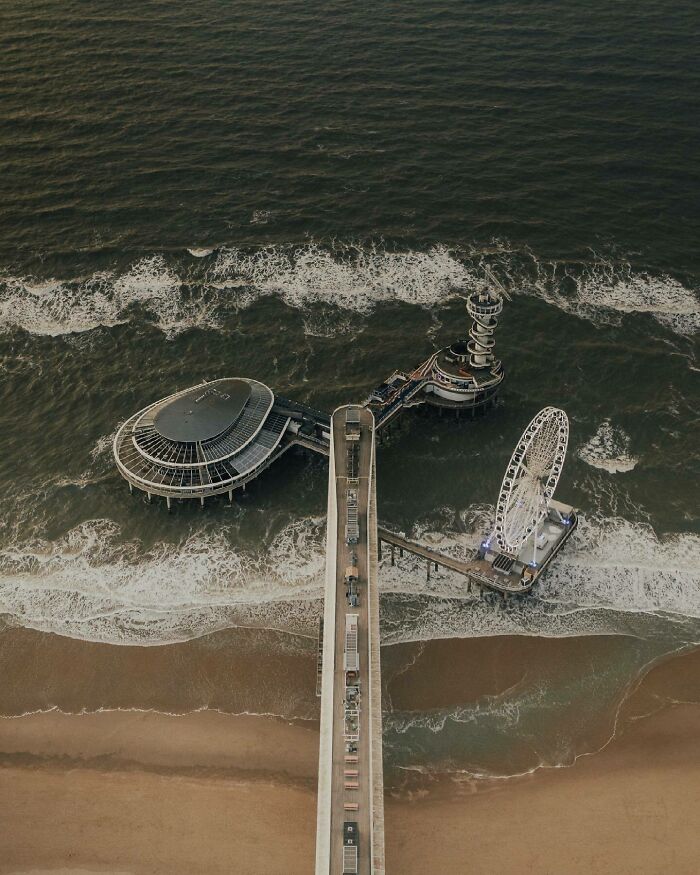 Aerial photo showing a pier extending into the sea with a Ferris wheel and modern buildings.