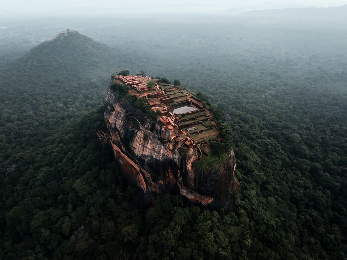 Aerial view of a lush green landscape with a historic rock fortress on a plateau.