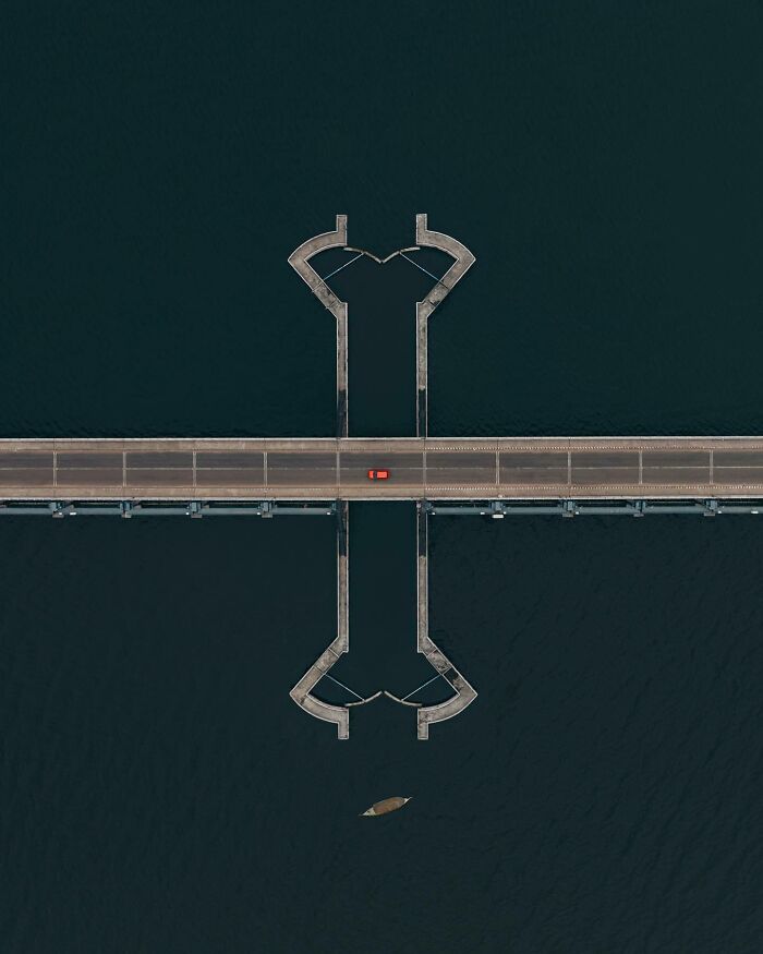 Aerial photo of a bridge over water with a single red car, showcasing the world from a different angle.
