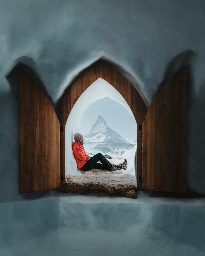Individual in red jacket viewing mountains through a snow-framed archway.
