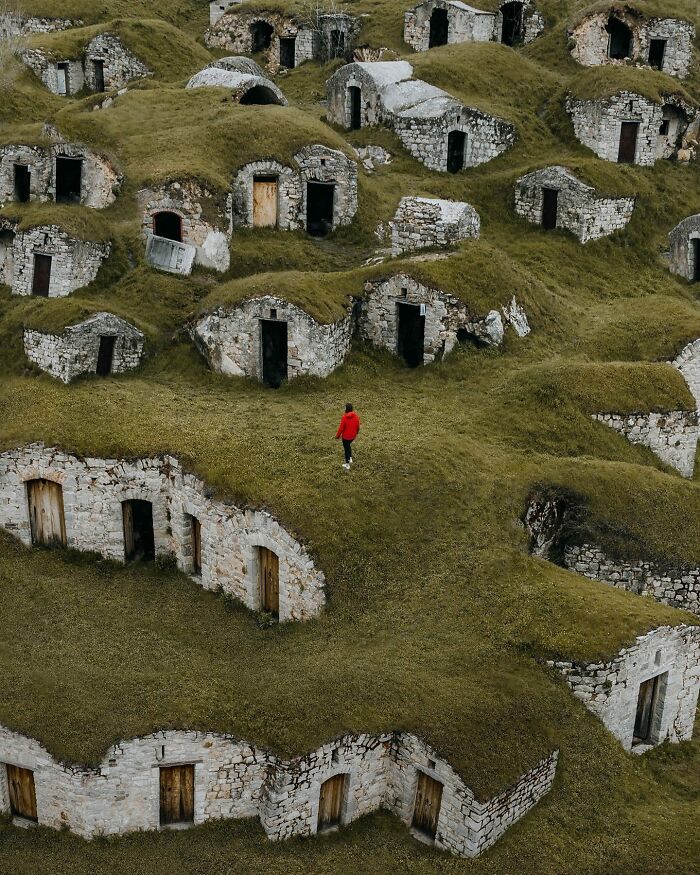 Aerial photo of unique stone structures with a person in a red coat walking on grassy hills.