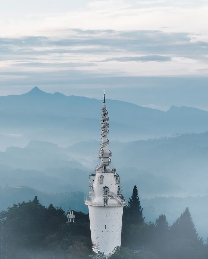 Aerial photo capturing a tall, spiral tower surrounded by misty mountains and forests.