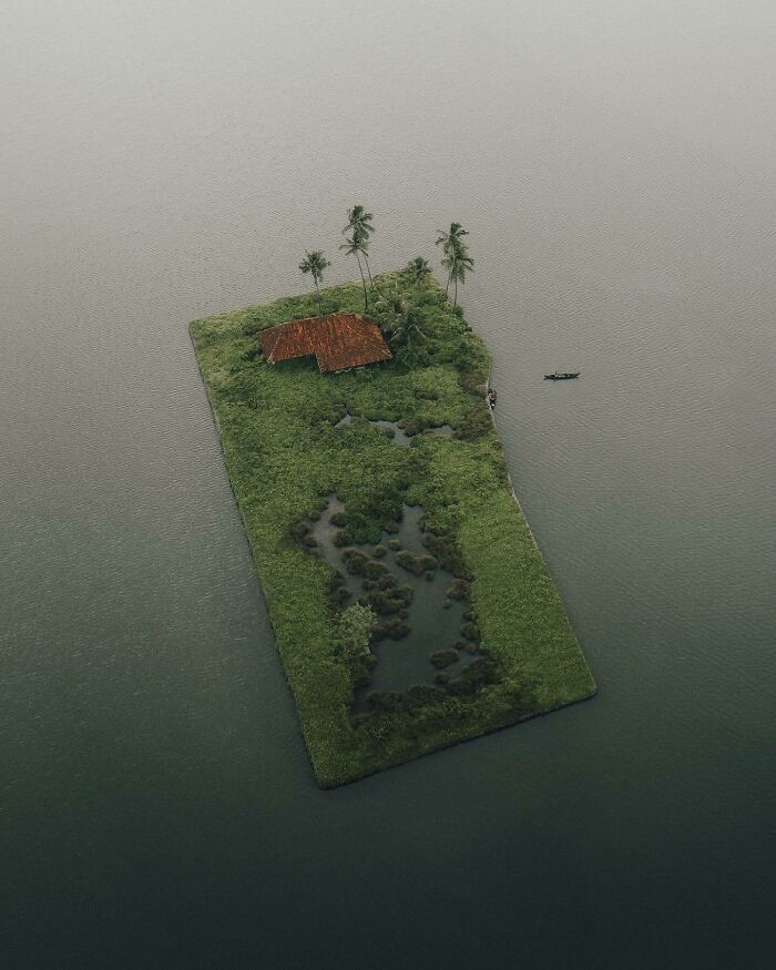 Aerial photo of a small island with a red-roofed house and palm trees, surrounded by water.