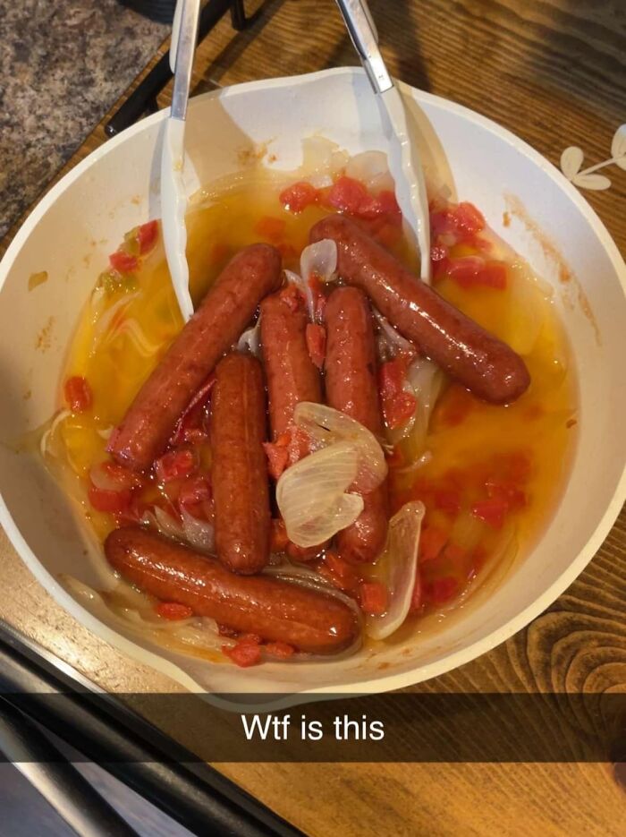 Unappetizing potluck dish of hot dogs, onions, and tomatoes in a white bowl with tongs, labeled "W*f is this."