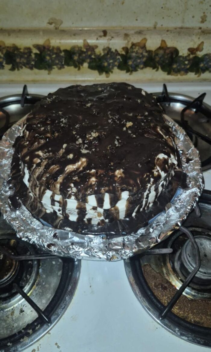Messy chocolate-drizzled cake on a stove, highlighting a potluck disaster.