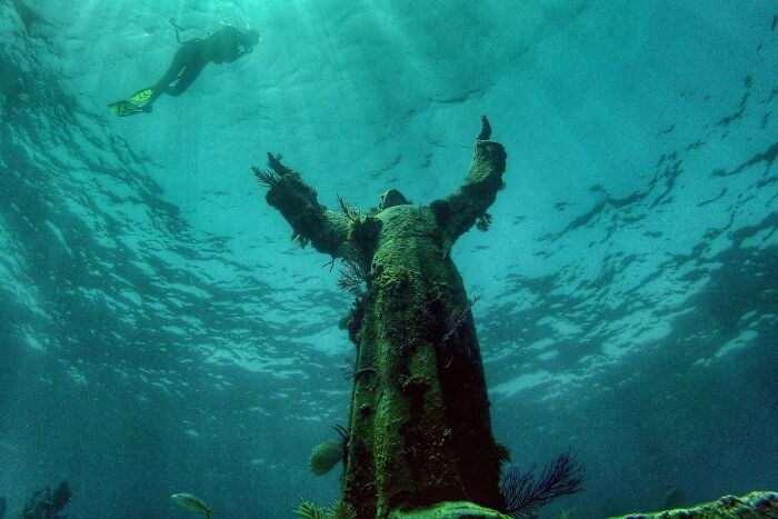 Underwater diver near a large statue in the ocean, showcasing strange oceanic discovery.