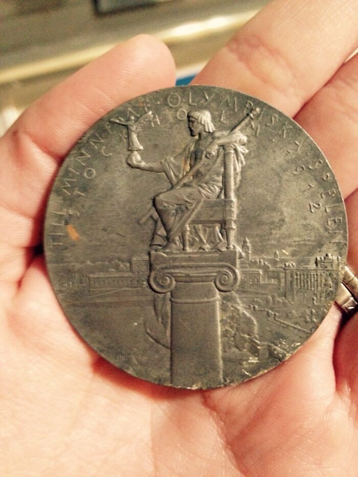 A hand holding an ancient artifact medallion depicting a seated figure holding a torch.
