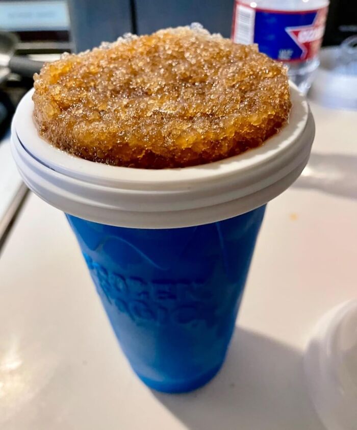 A blue frozen drink cup with a slushy brown beverage overflowing the lid.