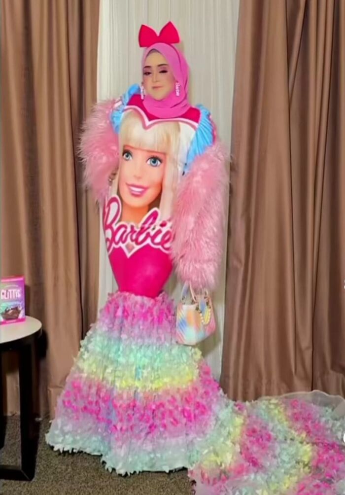 Person in a brightly colored, Barbie-themed outfit with pink and rainbow accents, posing against a curtain backdrop.