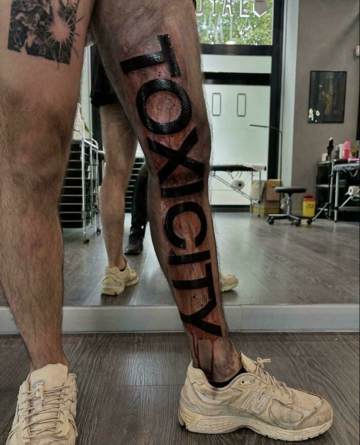 Leg tattoo fail with the word toxicity in bold black letters covering the entire calf, showcasing a wild tattoo fail.