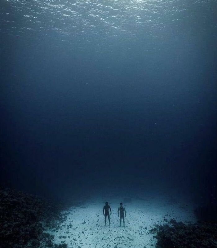 Two divers standing on the ocean floor surrounded by darkness, capturing strange oceanic depths.