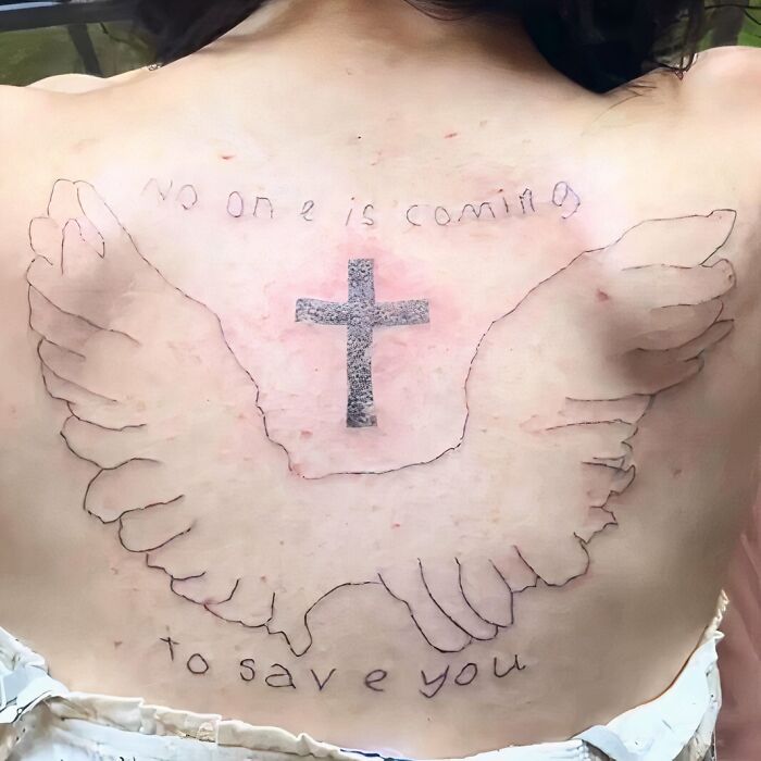 Back tattoo with wings, cross, and handwritten text; example of a permanent mistake inked on bodies.
