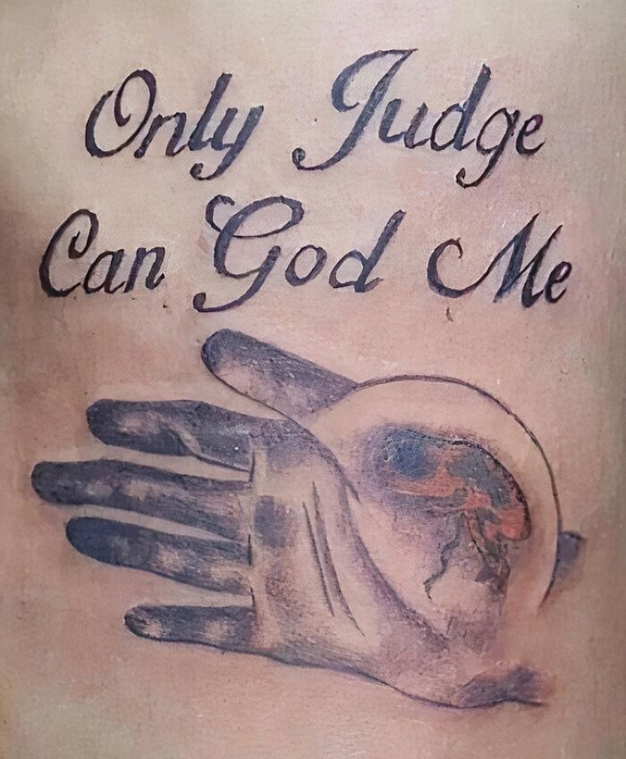 Tattoo mistake with the text "Only Judge Can God Me" alongside a hand and eye design on skin.