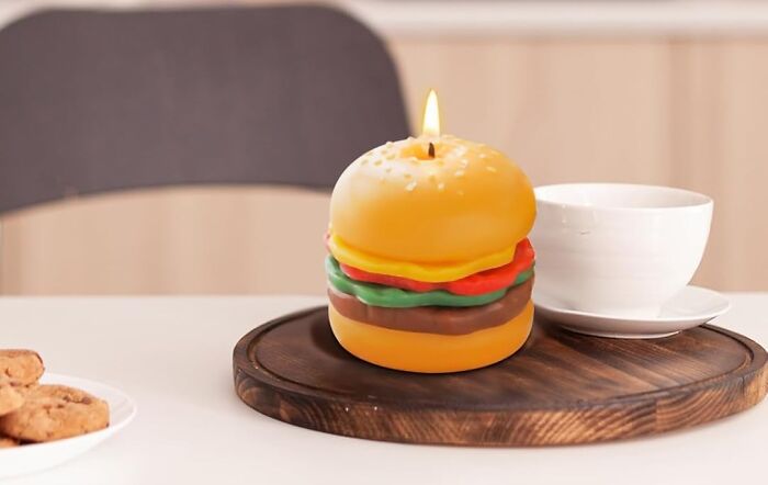 Burger-shaped candle masterpiece on a wooden tray next to a white cup.