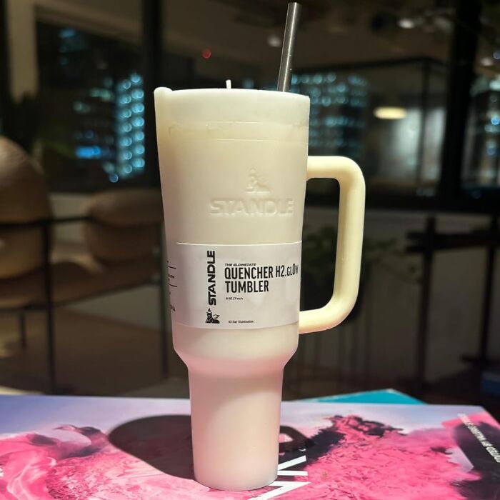 Innovative candle shaped as a white tumbler with handle, detailed label, standing on a table indoors.