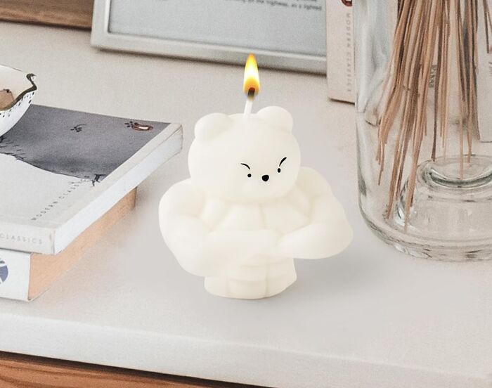 Artistic bear-shaped candle, sculpted in wax, lit on a cozy tabletop setting with books and decor.