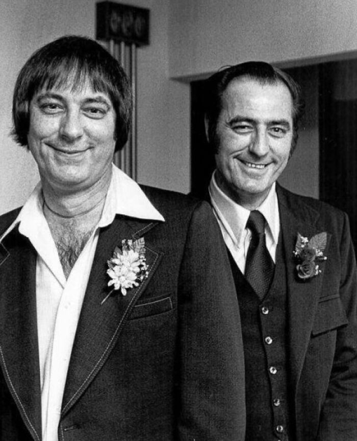 Two men in suits with boutonnieres, smiling at the camera, capturing a historical coincidence moment.