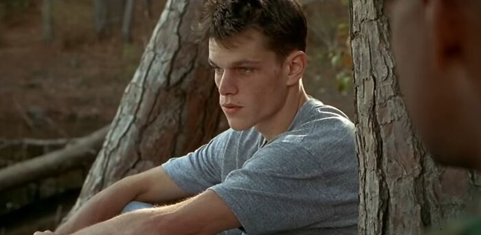 Young actor sitting against a tree outdoors, portraying a difficult role with intense and thoughtful expression.