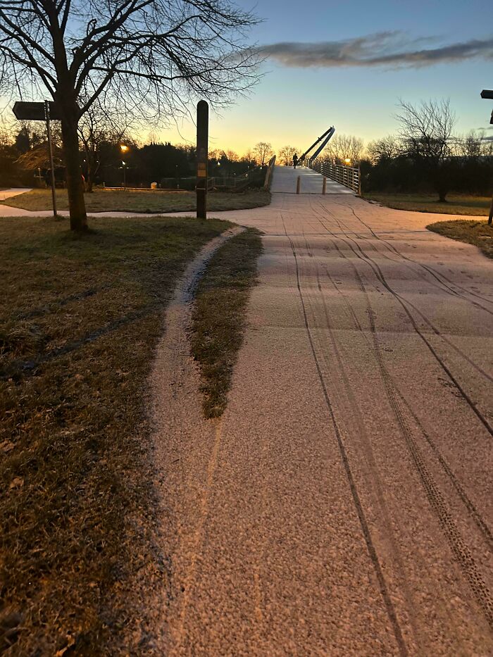 Path ending abruptly at a bridge with poor city planning evident, surrounded by trees at sunset.