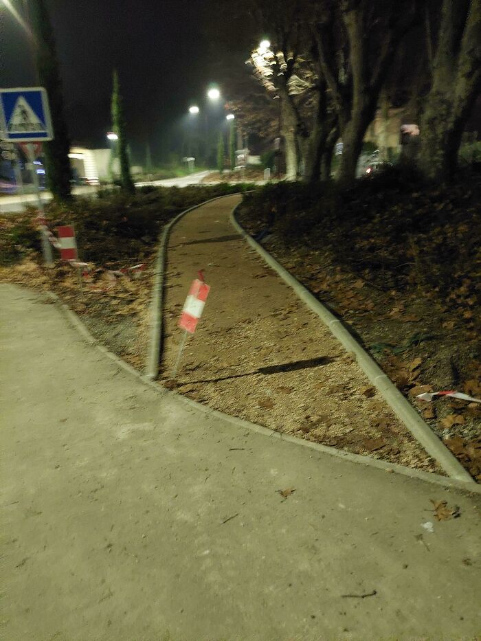 Curved pedestrian pathway with city planning oversight, marked by warning signs at night.