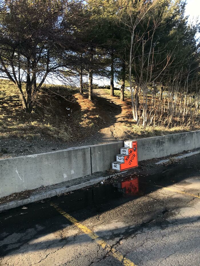 Path crossing a concrete barrier with a misplaced road work sign, showing poor city planning.