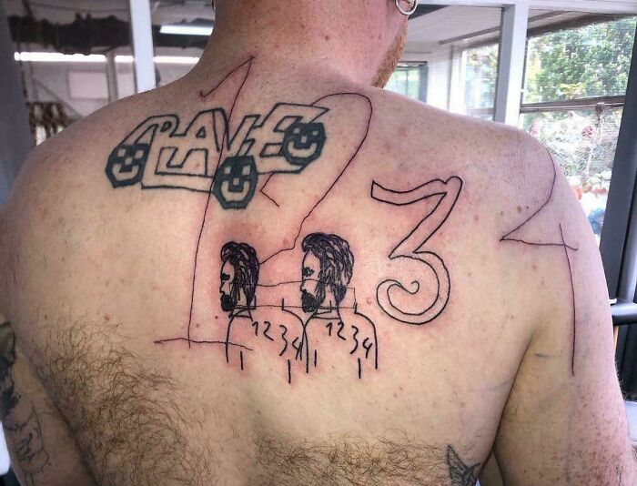 Tattoo fail on upper back with random numbers, faces, and blocky letters in a chaotic design.
