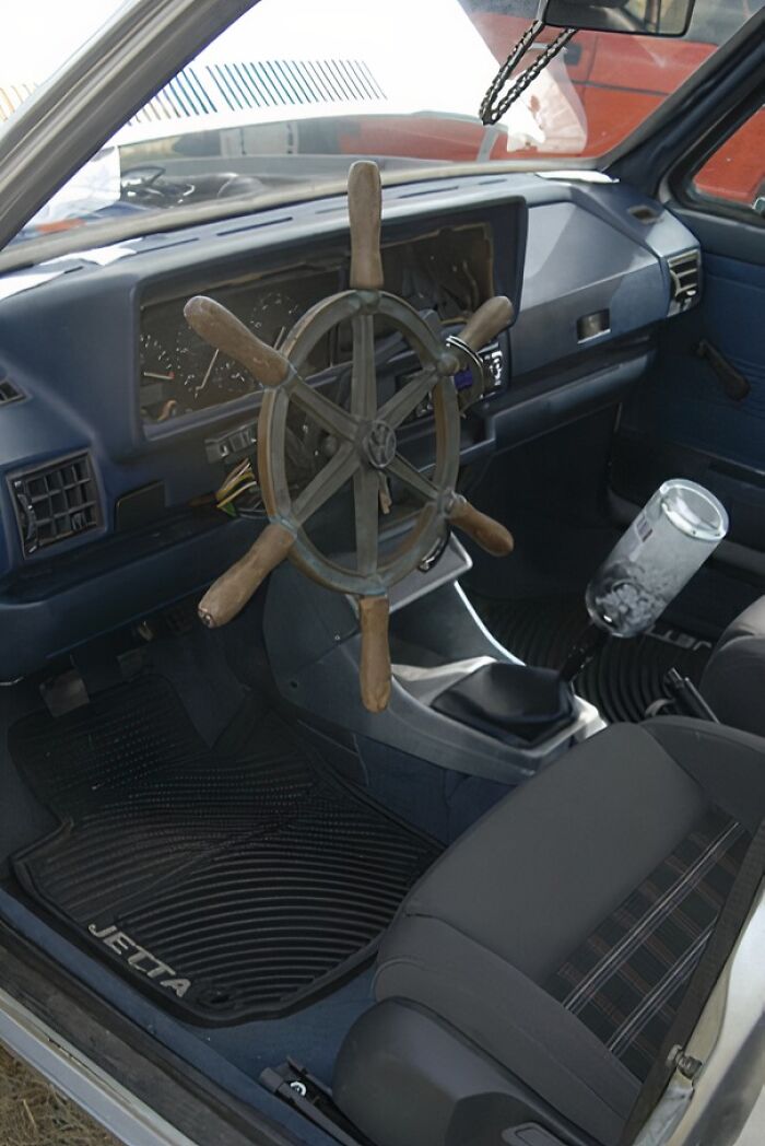 Car interior with a ship's wheel used as a steering wheel, illustrating a humorous repair fail.