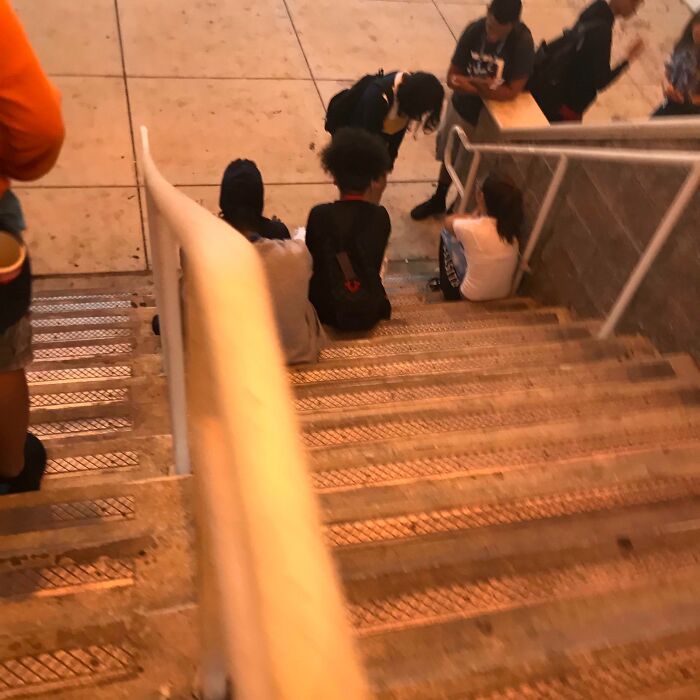 People sitting on stairs, blocking passage, showing lack of basic etiquette.