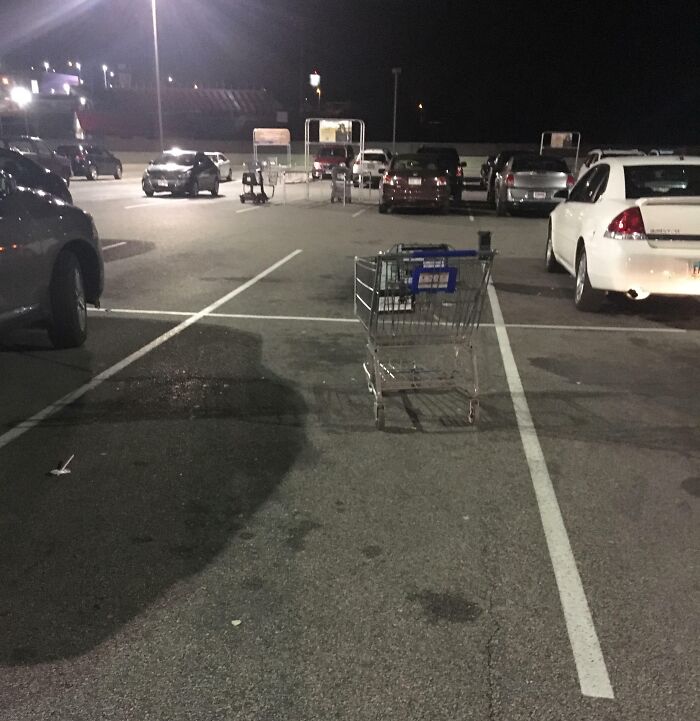 Shopping cart left in a parking spot at night, lacking basic etiquette.