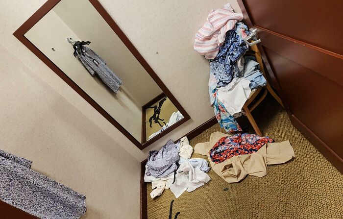 Messy fitting room with clothes scattered on the floor and chair, reflecting a lack of basic etiquette.