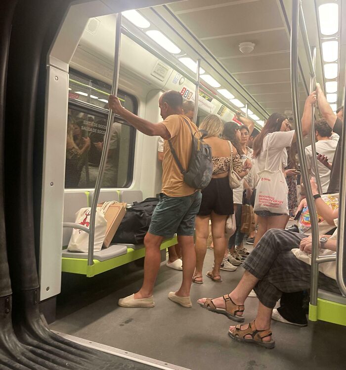 People standing and sitting in a crowded subway, some not following basic etiquette.