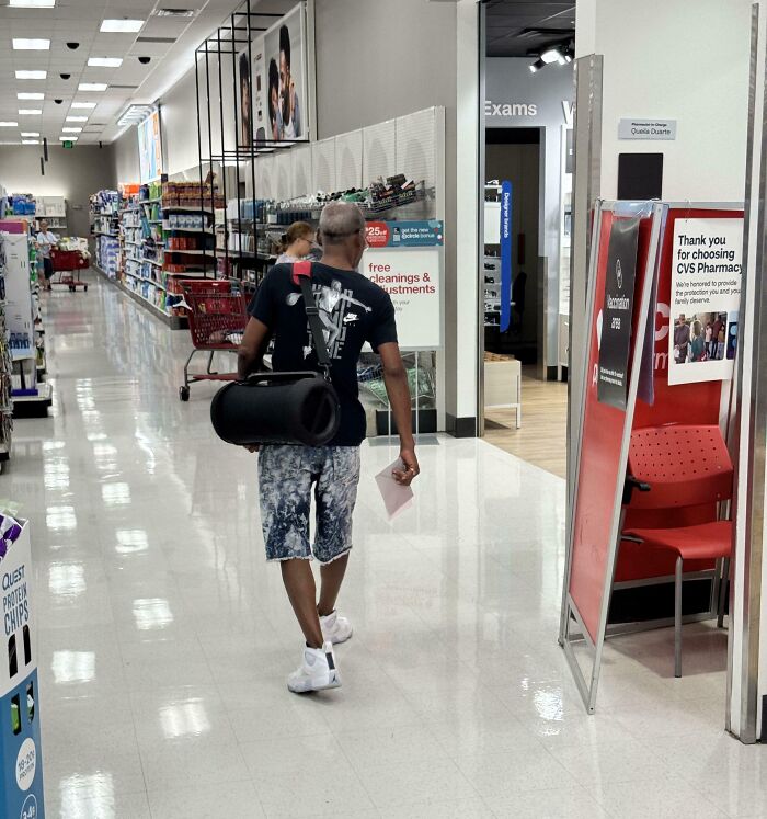 Man in store with yoga mat, casually dressed, demonstrating lack of basic etiquette by walking without shoes.