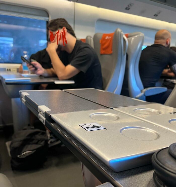 A person on a train occupying extra seats with a phone, demonstrating a lack of basic etiquette.