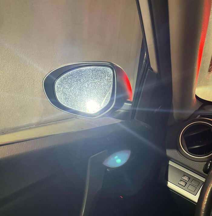 Car mirror reflecting bright light, highlighting lack of basic etiquette in driving.