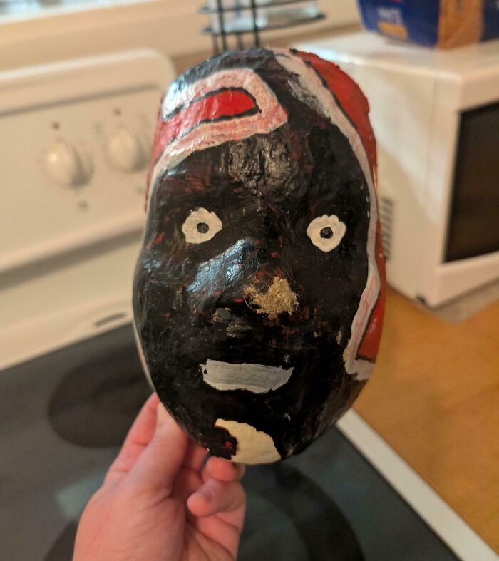 Hand holding a creepy painted mask found hidden in a home.