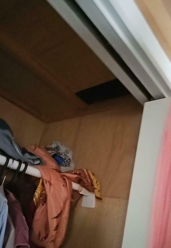 A hidden compartment in a closet ceiling, discovered after moving in, with clothes hanging nearby.