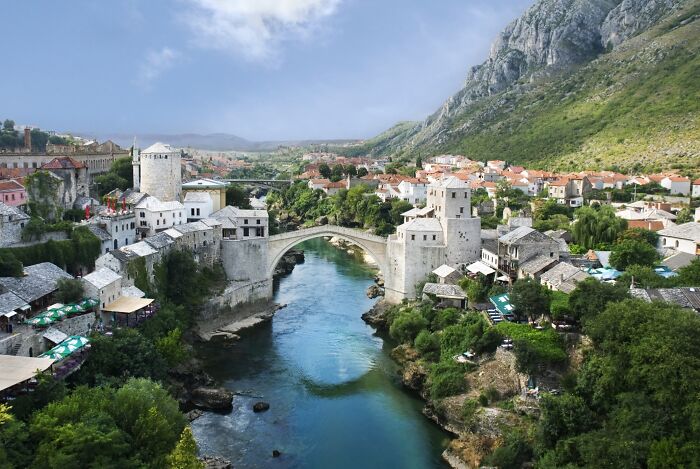 Scenic river with a historic bridge, showcasing an architectural wonder against a backdrop of mountains and charming town.
