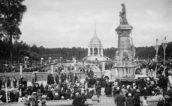 Crowd gathered around a historic European monument in a black and white photo showing life in Europe 100 years ago.